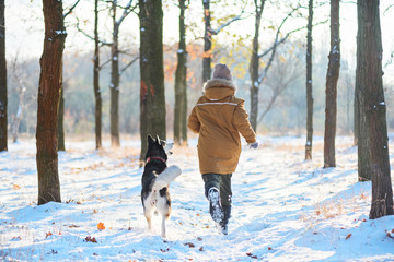 Wall Mural - Back view of running boy with husky on a distillation in a winter park