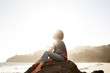 © Trinette Reed/Stocksy - Portrait of mixed race woman sitting on a rock at the beach
