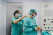 © MyMicrostock/Stocksy - Medic assistant putting the gown to surgeon in the operating room