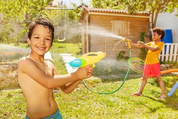 Boy with friend shoot water pistols on summer day