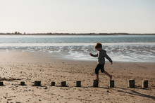 Side View Of Child Balancing On Log Pilings On Beach