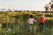 © Cavan Images - Little girl and boy holding hands walking away into a field