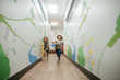 © Cavan Images - Two little girls smile and run down a mural covered hall in school