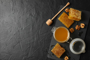 Walnut, honeycombs, jar with honey and dipper on black background, copy space