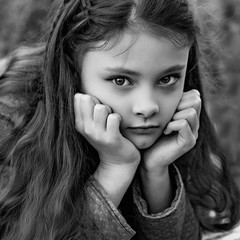 Wall Mural - Unhappy kid girl with beautiful hair looking sad. Hands under the face. Closeup portrait. Black and white.