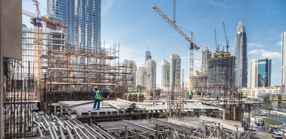 Laborers working on modern constraction site works in Dubai. Fast urban development consept. - obrazy, fototapety, plakaty 