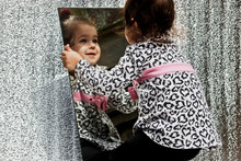 A Small Child With A Happy Look Of Face Looks At Himself In The Mirror Close-up. The Kid Shows Versatile Emotions In The Mirror.