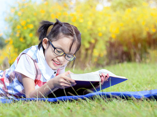 Wall Mural - Cute little girl with glasses reading book at park in summer sunset light