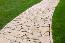 Flagstone Footpath In A Park With A Green Lawn Goes Into Perspective On A Sunny Summer Day, Close-up Of Paving Stone Tiles.