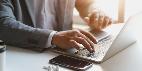Close-up view of young businessman working on his project while typing on laptop computer