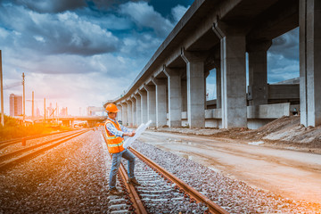 A engineer under inspection and checking construction process railway work on rail train station by Blueprint  on hand . Engineer wearing safety uniform and safety helmet in work.