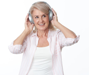 Wall Mural - Cheerful 50 years old woman in headphones is listening to music. Isolated