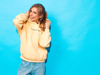 Portrait of young beautiful smiling girl in trendy summer hipster yellow hoodie.Sexy carefree woman posing near blue wall. Positive model having fun