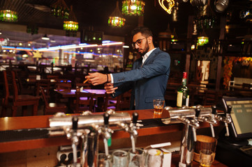 Wall Mural - Handsome well-dressed arabian man with glass of whiskey and cigar posed at pub.