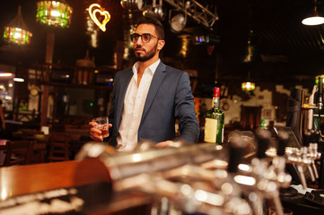 Wall Mural - Handsome well-dressed arabian man with glass of whiskey and cigar posed at pub.