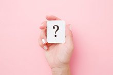 Card Of Question Mark In Young Woman Hand On Pastel Pink Background. Concept Of Plans, Thoughts Or Other Good Ideas For Making Decision. Closeup.
