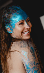 Wall Mural - Portrait of beautiful happy woman with blue sparkles on her face. The concept of freaks and aliens. People are different from others. Individuality