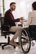 © LIGHTFIELD STUDIOS - back view of disabled businesswoman gesturing while talking to business partner in office