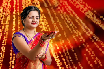 Wall Mural - Indian woman in traditional sari and holding oil lamp in Hand celebrating Diwali or deepavali, fesitval. 