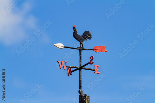 Cockerel Rooster weather vane, wind vane, weathercock against blue sky. Cast iron wind direction instrument, with letters for compass points, painted black red and white. Dublin, Ireland