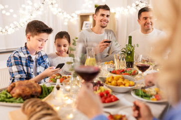 Poster - technology, holidays and people concept - happy children with smartphone at family dinner party