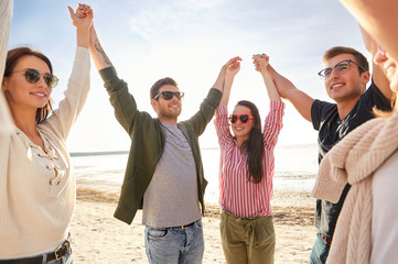 Wall Mural - friendship, leisure and people concept - group of happy friends holding hands on beach in summer