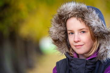 Pretty young girl in furry hood with blurry fall colors in the background