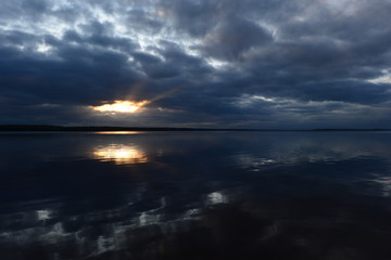 Wall Mural - Cloudy blue sky at sunset in a bright beautiful glow of the sun's rays from the heavenly  sunlight clouds clearance reflects in the lake water
