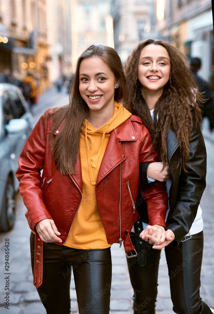 portrait of young female friends in colored leather biker jackets and hoodies holding hands while walking down the street. Stock Photo | Adobe Stock portrait of young female friends in colored leather biker jackets and hoodies holding hands while walking down the street. Stock Photo | Adobe Stock