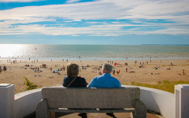 couple assis de dos face à l'océan et une plage avec du monde en Loir atlantique à Saint Michel Chef Chef