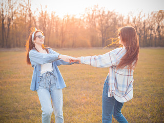 Two young women dancing on the autumn field at sunset