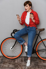 Sticker - Full length image of confused woman holding smartphone by bicycle