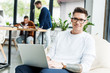 © LIGHTFIELD STUDIOS - young businessman using laptop and smiling at camera while working near colleagues in office