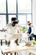 © LIGHTFIELD STUDIOS - african american businessman squatting on table while using vr headset, and colleagues working in office