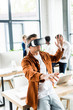 © LIGHTFIELD STUDIOS - young businessman using vr headset and gesturing while multicultural colleagues working in office
