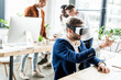 © LIGHTFIELD STUDIOS - young businessman using vr headset and touching something with finger while multicultural colleagues working in office