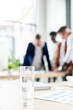 © LIGHTFIELD STUDIOS - selective focus of glass with water on desk near businesspeople standing at workplace in office