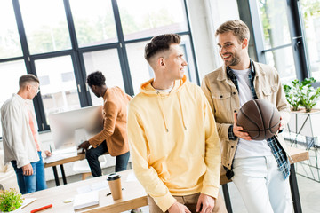 smiling businessman holding volleyball ball while talking to colleague in office