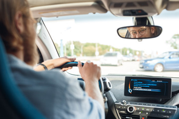 Young adult man sitting in car, looking at rear view mirror