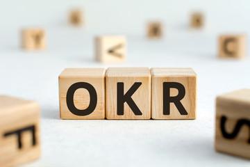 OKR - acronym from wooden blocks with letters, abbreviation OKR Objectives and Key Results concept, random letters around, white  background