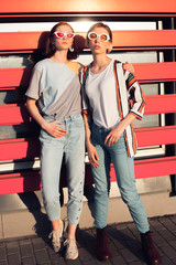 Wall Mural - Two fashionable young women posing in the ciry on the orange background