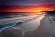 Sunrise at sandy beach in Baabe, slow incoming waves, morning sky with orange sunrise, Ruegen island, Baltic Sea, Germany.