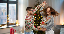Celebration, Fun And Holidays Concept - Happy Couple Wearing Ugly Sweaters Dancing At Christmas Party