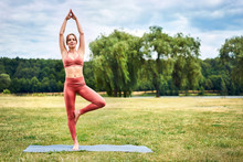 Athletic Woman Doing Tree Yoga Pose During Training Session In The Park