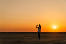 Germany, Schleswig-Holstein, Sankt Peter-Ording, Woman Taking A Picture On The Beach At Sunset