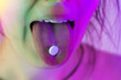 Female tongue with a pill on it close-up in neon light.