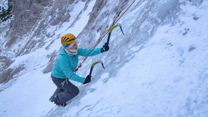 CLOSE UP: Young female alpinist scales up dangerous frozen waterfall in the Alps