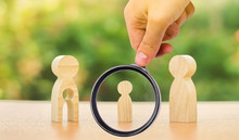 A Magnifying Glass Looks At A Child’s Figure Stands Between Father And Mother. The Child Chooses Which Parent To Live With After Their Divorce. Guardianship Over Child. Interest Of Child