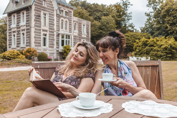 couple of mature friendly women on vacation drinking tea and reading a book outdoors