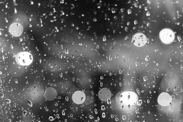 Wall Mural - Black and white mood and tone, close up and macro view of raining water drop on glass window and blur background with circle round light bokeh. 
